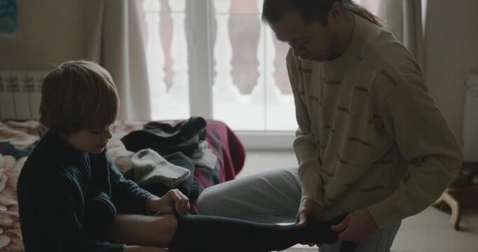Man puts warm clothes on child. Dad help child to dress at home. 4K 10-bit