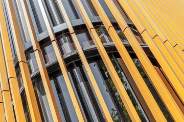 Obraz premium Vertical yellow louvers covering curved building facade with windows
