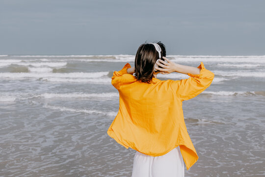 Woman wearing yellow shirt listening to music at beach
