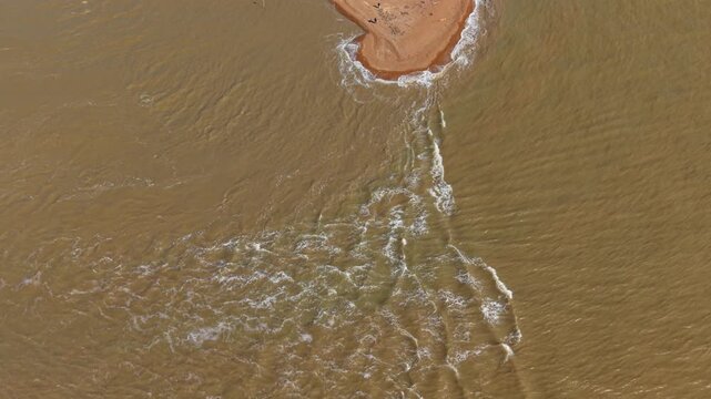 Top down aerial view of sand bank and tidal flow in a British estuary during ebb tide with waves rushing in.