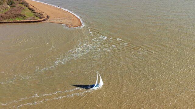 Aerial drone view of a small yacht sailing against the tide in the Deben Estuary, Felixstowe Ferry, UK