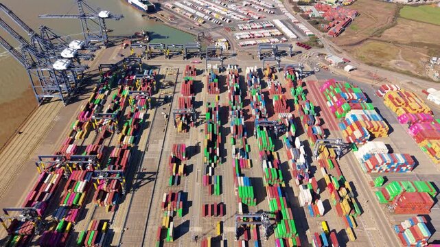 Top-down aerial footage of Felixstowe industrial shipping port with cranes loading a commercial container ship for international logistics