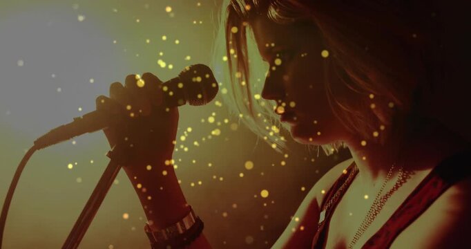 Teen singer gripping mic, leaning in, singing music while particles framing profile by stage light