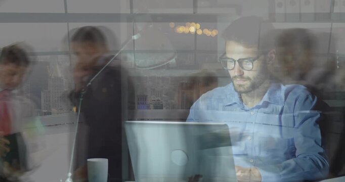 Seated man typing at laptop blurred staff passing forming layer, pausing to sip and resuming work