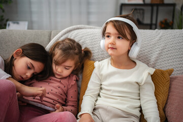 Obraz premium Young sisters focusing on digital tablet and headphones at home