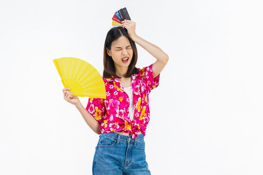 Young woman is stressed feeling hot and tired while holding a yellow hand fan and holding credit card on white background.