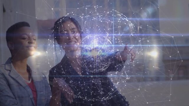 Two colleagues viewing hologram globe projecting near window, pointing nodes, proving tech teamwork