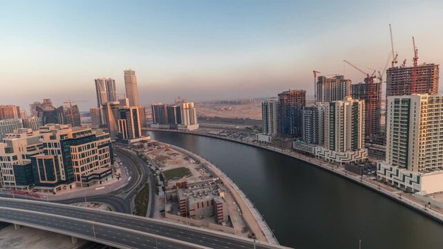 Modern skyscrapers and highway bridge over the water canal in Dubai Business Bay. Aerial panoramic view during sunset and evening time-lapse.