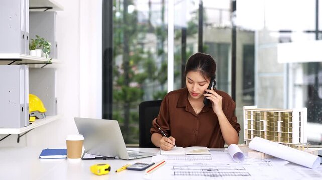 Female Civil Engineer Construction professional reviewing shop drawing of structural floor plan  and communicates on smartphone in an office.