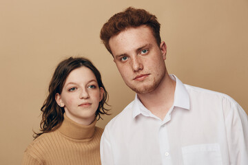 Obraz premium Young man and woman with serious expressions pose together against beige background. Casual clothing and natural look create a calm, neutral mood for portrait or lifestyle concept.