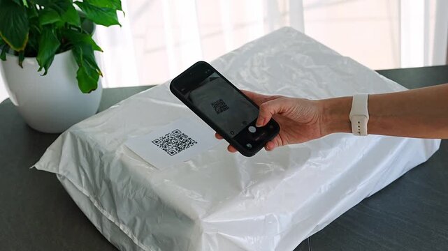 Person scanning QR code on parcel with smartphone camera for delivery tracking at home. Contactless technology mobile app and digital service concept.