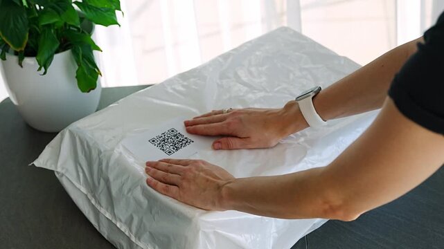 Person placing QR code label on parcel before shipping at home. Preparing package for delivery with digital tracking and logistics process concept.