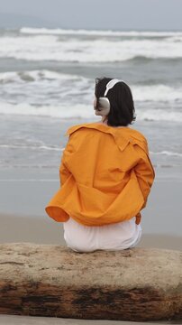 Static slow motion tracking pan shot of woman sitting and listening with headphones on driftwood beach shore