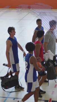 Vertical video: Male players walking off court after game, passing basketball, bags, water bottles