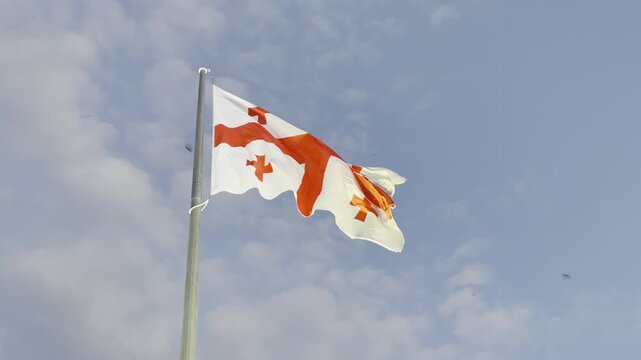 National flag of Georgia waving in the wind against a blue sky with light clouds. High-quality video footage of the Georgian state symbol on a flagpole. Perfect for news and travel content.