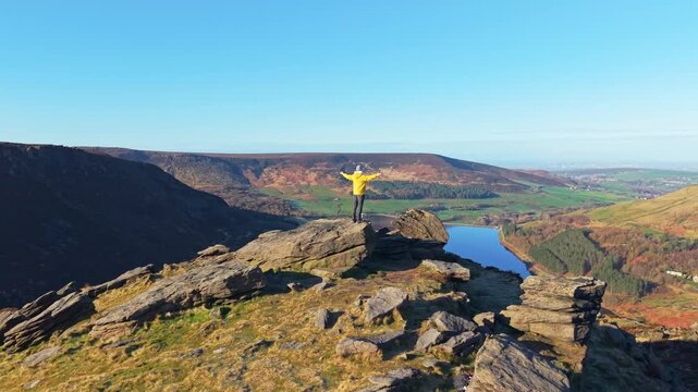 A man demonstrating stunning view from the rock above Dovestone reservoir. Dove Stone Reservoir lies at the convergence of the valleys of the Peak District National Park, Greenfield, UK.