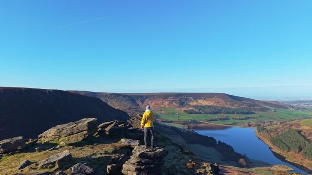 A man demonstrating stunning view from the rock above Dovestone reservoir. Dove Stone Reservoir lies at the convergence of the valleys of the Peak District National Park, Greenfield, UK.