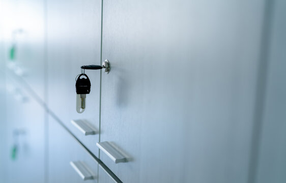 Locker with key in office room. Filing cabinet lock with key for safety and security system in public facility. Secure lock system for document files in business office. White locker door for storage.