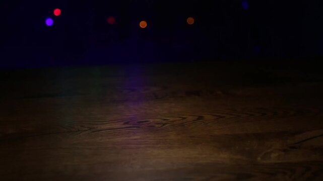 Wide empty wooden tabletop at night remains still beneath colorful bokeh lights as faint reflections drift across the surface, forming a festive background with horizontal copy space for products.