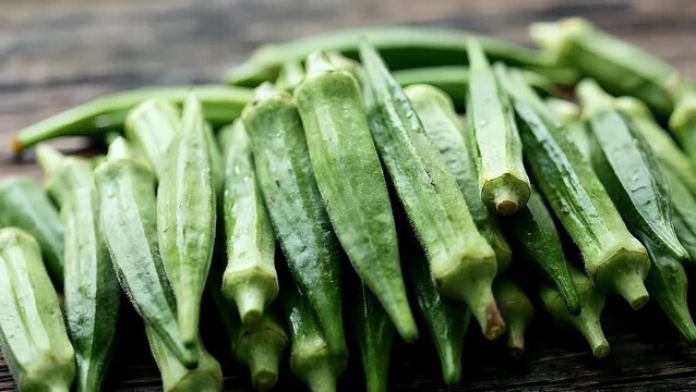 Fresh green okra pods piled on a rustic wooden table background