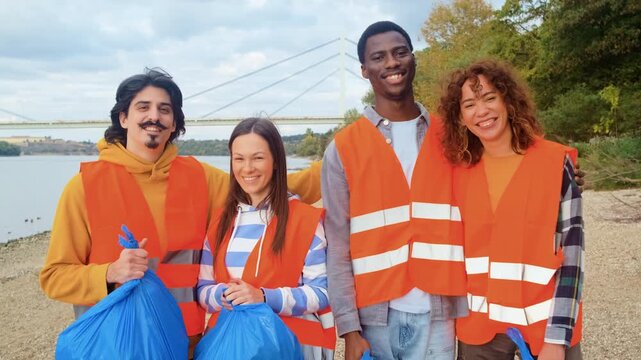 Portrait of a group of volunteers standing on the riverbank looking at camera after collecting plastic waste.