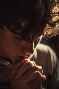 Teen praying with head bowed and soft lighting across face showing emotion and quiet trust in God through prayer