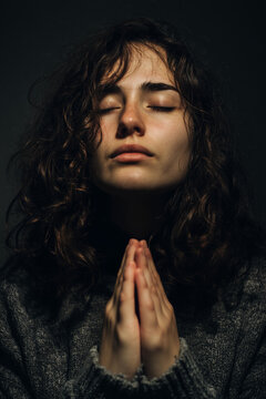 Young praying woman with curly hair and eyes shut in quiet moment of deep Christian belief and inner peace