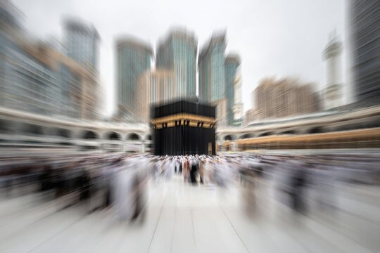 Crowds circumambulate a central cubical structure surrounded by modern skyscrapers with motion blur effect