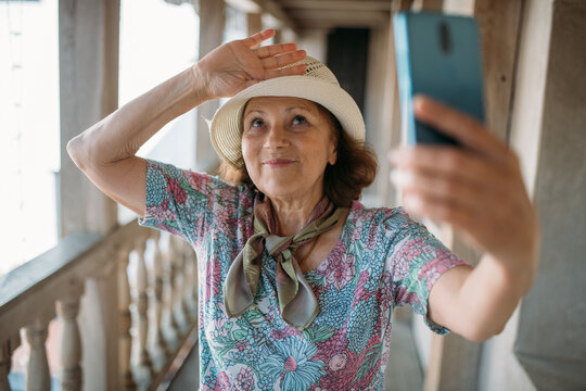 An elderly, contented woman takes a guided tour of the park near the ancient castle. The pensioner examines the historical architecture and takes a selfie with her phone.