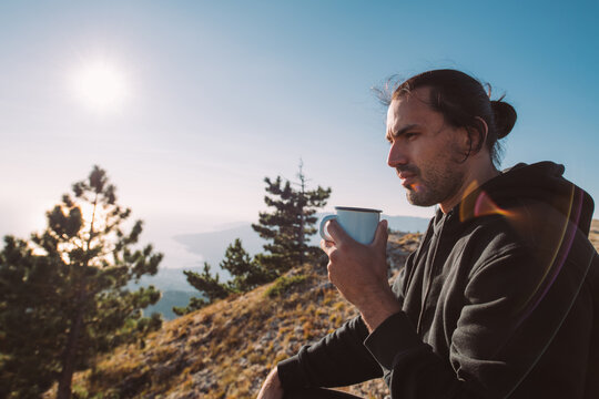 Male tourist drinks tea on the top of the mountain at sunrise