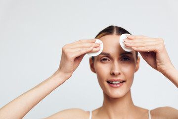 Young woman with clear skin removing makeup with cotton pads on white background. Concept of skincare, cleansing, beauty routine, and healthy lifestyle. Soft lighting highlights natural look. © SHOTPRIME STUDIO