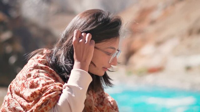 Portrait of beautiful young Indian woman sitting near mountain river in Zanskar, Ladakh, India. Outdoor portrait of graceful Indian woman. Travel, vacation and holidays concept.