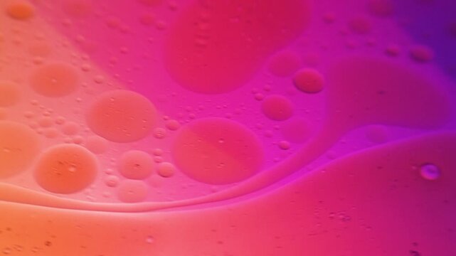 Macro close-up of colorful bubbles on a liquid surface with a gradient of pink, purple, and orange hues.