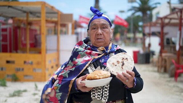 Proud elderly woman wearing traditional mapuche clothing and holding a plate of fresh homemade bread