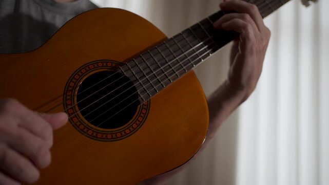Close-up of Musician Hands Playing Acoustic Guitar. Detailed view of fingers strumming strings on a wooden acoustic guitar. Focus on the soundhole and strings with a blurred background