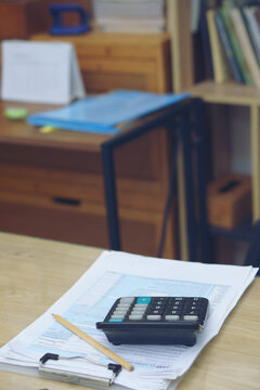 Calculator with pencil on financial documents and tax forms on a wooden business desk. Concept of accounting, tax season, planning, and financial management in home office-vertical