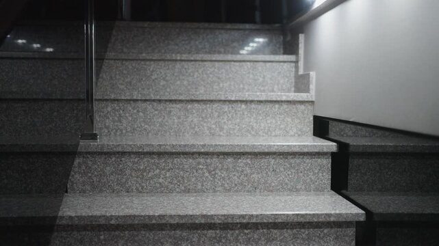 Jack Russell Terrier Dog Walking Down Granite Stairs at Night. White and brown dog carefully descending modern stone steps. Dimly lit indoor scene showing pet behavior and home interior at night