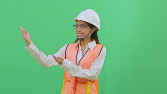A female engineer in a white helmet pointing towards an imaginary safety sign. Directing attention to rules or procedures on a green screen background.