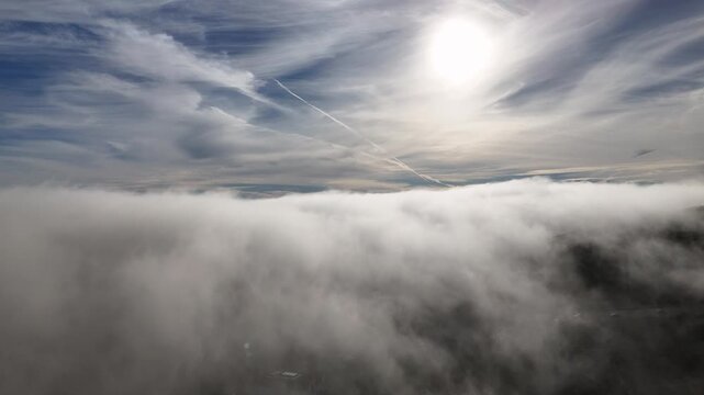 Aerial view of fluffy white clouds meeting a blue sky streaked with wispy cirrus clouds and a bright sun, creating a surreal, ethereal landscape, Malibu, California, United States.