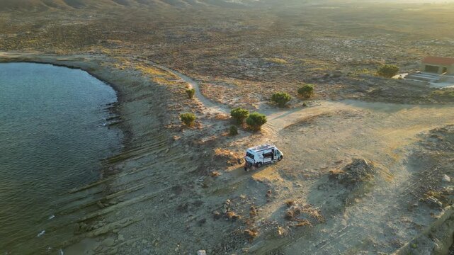Aerial drone view of a parked campervan at beach Louri on Limnos Island, Greece. Remote Mediterranean coastal landscape with turquoise sea, rocky shoreline, and peaceful free camping atmosphere ideal