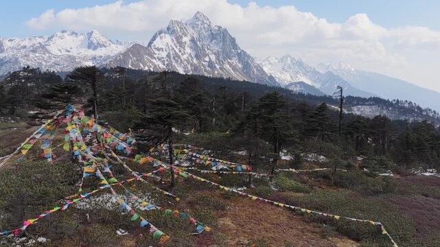 Aerial view of prayer flags strung across trees in Peacock Mountain, set against a backdrop of snow-capped peaks, Deqing, China.
