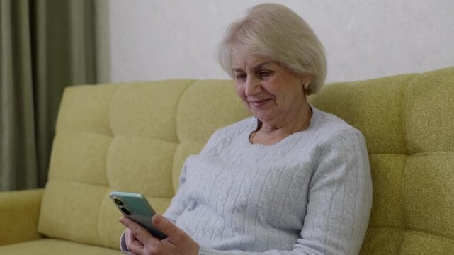 Senior woman enjoying social media. Older lady relaxing and exploring online content. Elderly woman comfortably scrolling through social media posts during tranquil evening at home