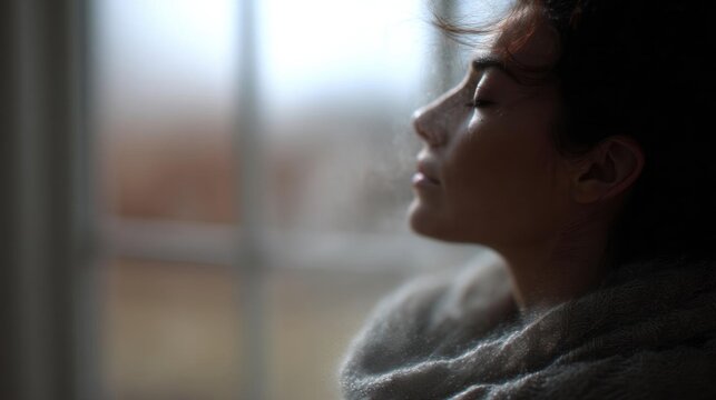 Close-up portrait of a young woman's face. she is looking out of a window with her eyes closed and her head tilted slightly to the side. the woman appears to be deep in thought or contemplation.