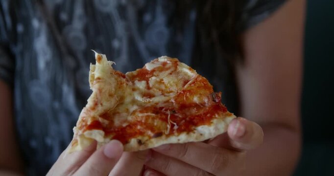 Closeup hands holding cheesy pizza slice, woman lifting slice with stretchy melted cheese, golden crust and tomato sauce visible, casual indoor dining, cozy indulgent mood, focus on texture