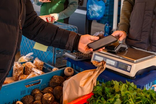 White hands paying card at scale, vendor weighing yams while customer completes contactless payment with wallet, exchange captured at outdoor stall, commerce and local food scene