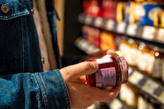 Man closely inspecting product label details. Male shopper scrutinizing ingredients on container in store. Male customer carefully reviewing smallprint ingredients on jar in grocery aisle