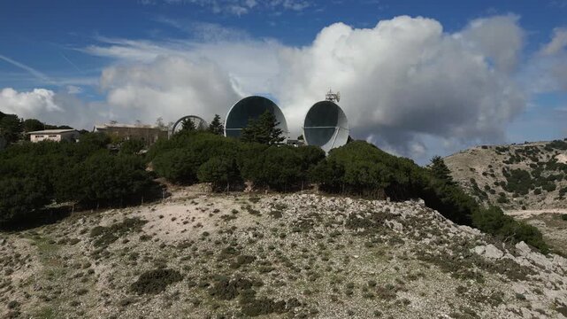 A remote satellite array on a rocky, wooded hillside under a dramatic sky.