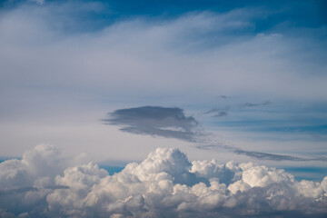 Fototapeta premium a dense, bright white wall of cumulus clouds at the bottom, with a unique, elongated dark grey cloud formation floating centrally beneath a soft layer of upper cirrus clouds.