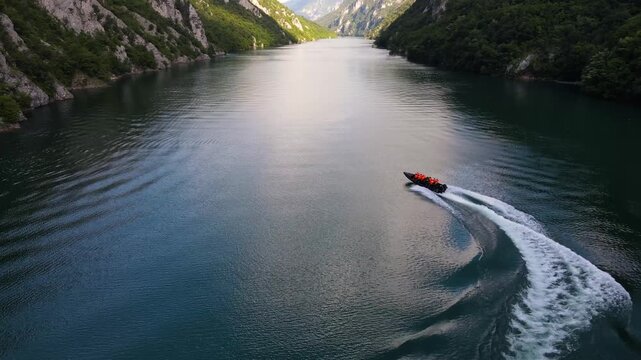 Aerial view of a red boat cutting through the calm, dark waters of Perucac lake, contrasting against the green mountains, Perucac, Zlatibor District, Serbia.
