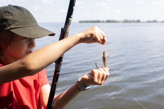 preteen boy caught a small fish on a fishing rod while standing by the river. Relaxation and favorite hobby by the water. Fishing vacation.